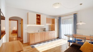 Cozinha moderna com armários de madeira, área de jantar com mesa e cadeiras, e um espaço de estar acolhedor com um sofá.