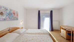 Quarto com cama, escrivaninha e janela com cortinas.