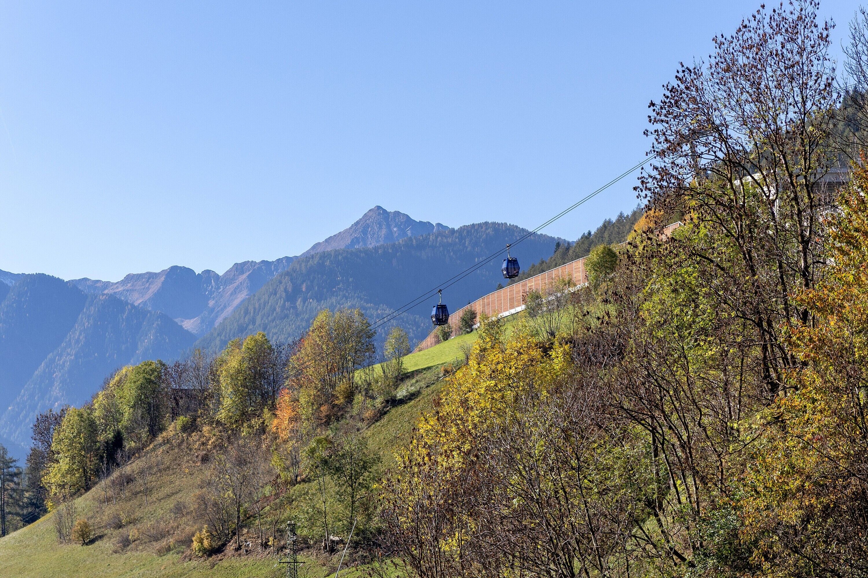 A cable car system in a mountainous area with trees and a clear sky.