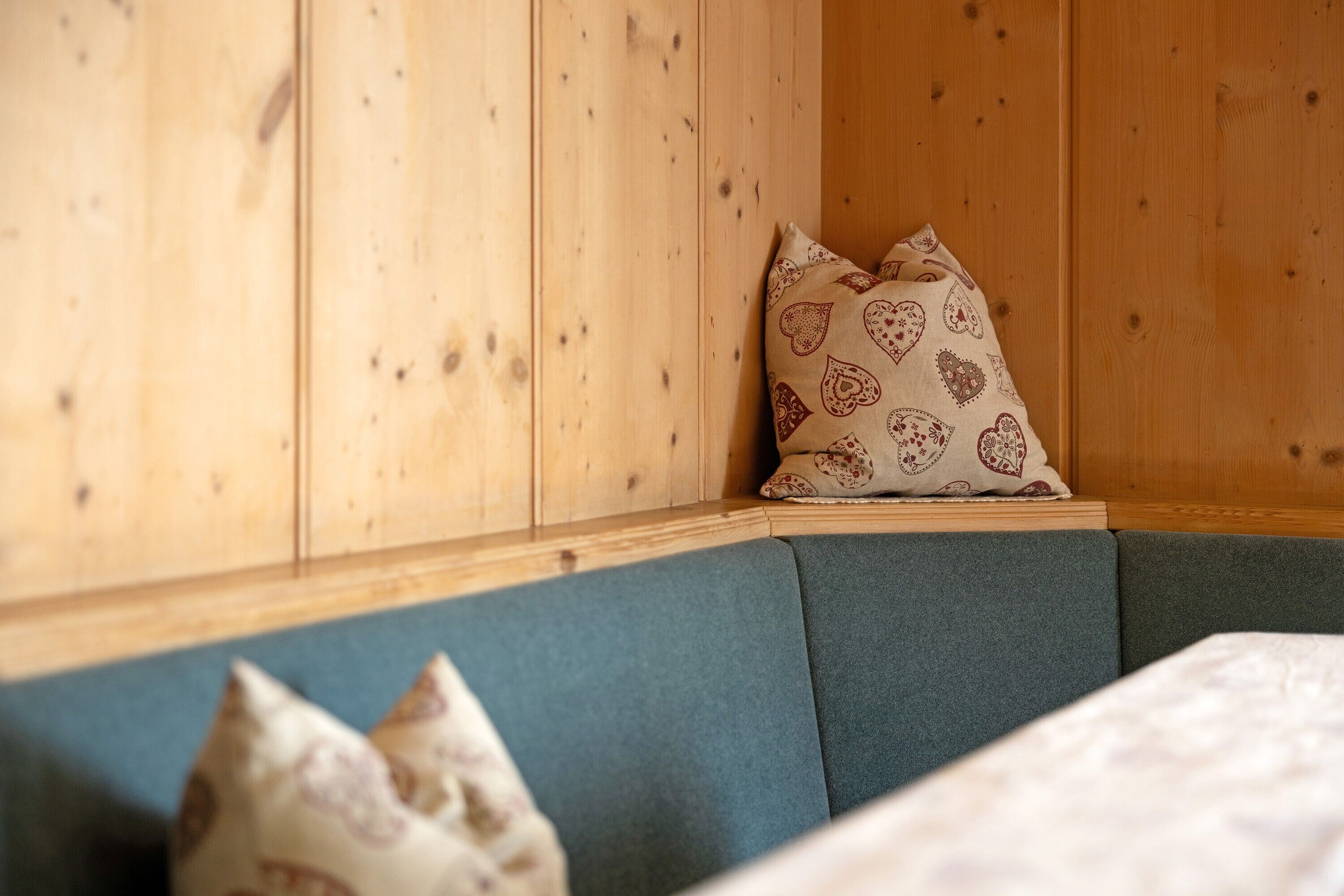 A corner of a room with wooden paneling, a green cushioned bench, and patterned pillows.
