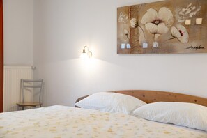 A bedroom with a wooden headboard, a bed with white pillows, a wall-mounted light fixture, and a floral painting.