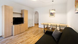 Ein modernes Wohnzimmer mit Flachbildfernseher, Holzkästen, einem Esstisch mit Stühlen und einem Sofa.