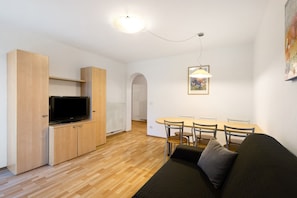 A modern living room with a flat-screen TV, wooden cabinets, a dining table with chairs, and a sofa.