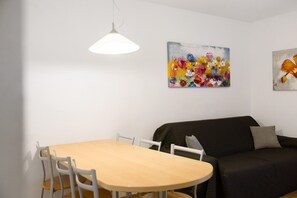 A room with a dining table, chairs, a sofa, and two paintings on the wall.