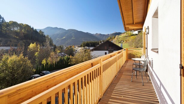 Une terrasse en bois offrant une vue sur les montagnes et un bâtiment blanc doté d  ’un balcon.