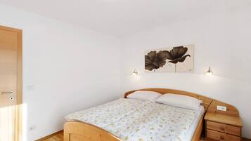 A bedroom with a wooden bed, a nightstand, a wall-mounted lamp, and a floral painting.