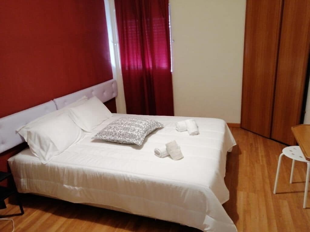 Una cama con sábanas blancas, un cojín estampado y toallas dobladas.