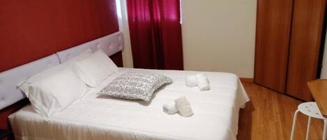 Una cama con sábanas blancas, un cojín estampado y toallas dobladas.