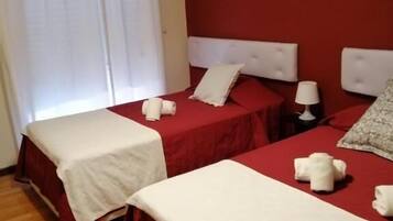 Ein Hotelzimmer mit zwei Betten, jeweils mit weißer Bettdecke und Kissen, einem Nachttisch mit Lampe sowie einem Fenster mit weißen Vorhängen.