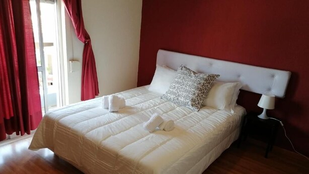 A neatly made bed with white bedding, a red wall, and a wooden floor. - Guest House RSA by Umbral (Loulé)