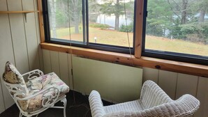 Ein Zimmer mit Holzwänden und einem großen Fenster. Zwei Korbstühle und eine Heizung sind vorhanden.
