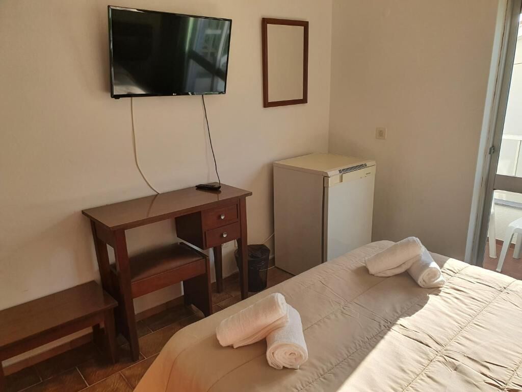 A hotel room with a bed, a desk, a television mounted on the wall, and a small refrigerator.
