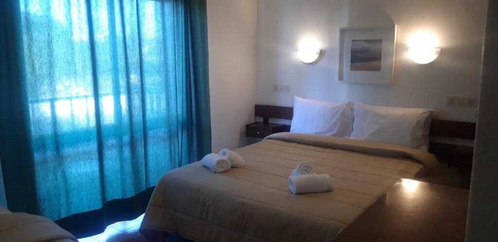 A hotel room with a bed, two bedside tables, a nightstand, a wall-mounted light, and a window with curtains.