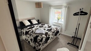 A bedroom with a bed, a hanging light, a window with curtains, and a floor lamp.
