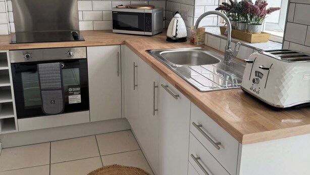 A modern kitchen with white cabinets, a stainless steel range hood, a microwave, a kettle, a toaster, and a sink.