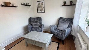 A living room with striped armchairs, a white coffee table, and a 'GOOD VIBES ONLY' sign on the wall.
