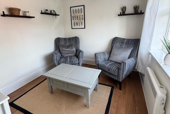 Ein Wohnzimmer mit gestreiften Sesseln, einem weißen Couchtisch und einem Schild an der Wand mit der Aufschrift 'GOOD VIBES ONLY'.