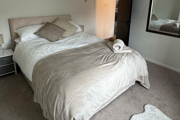 A neatly made bed with a patterned bedspread and pillows, a bedside table with a lamp, and a mirror on the wall. - Cottage - Sleeps 4 - Pets Ok - Patio - Parking (Middlewich)