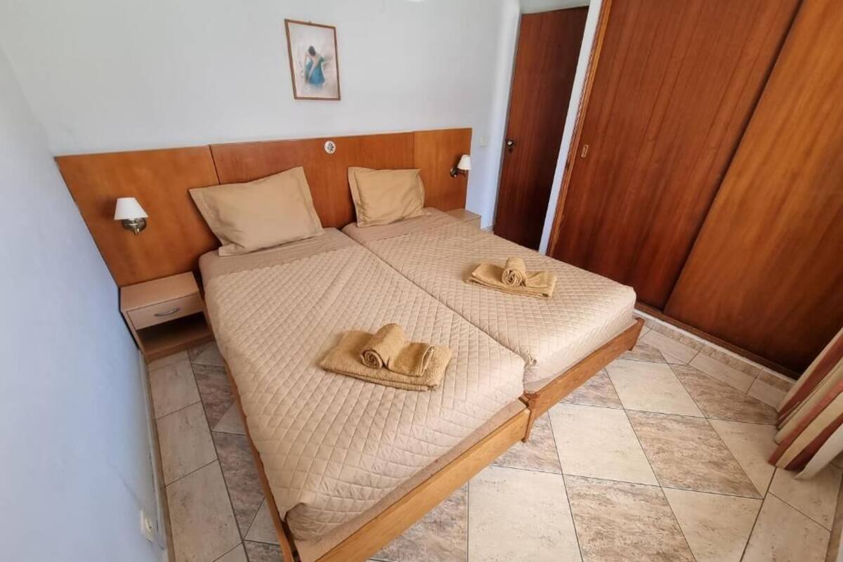 A double bed with a wooden headboard, two pillows, and a quilted bedspread. There are two bedside tables with lamps, a wooden wardrobe, and a framed picture on the wall.