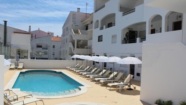 A swimming pool area with lounge chairs and umbrellas, surrounded by white buildings with balconies. - Cerro Atlântico by Umbral (Albufeira)