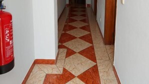A hallway with a checkered floor pattern, a fire extinguisher on the left, and wooden doors on the right. - Cerro Atlântico by Umbral (Albufeira)