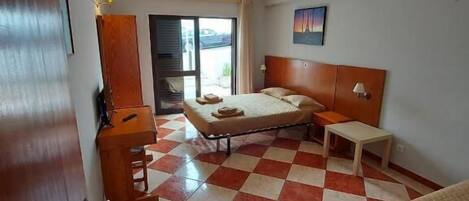 Quarto de hotel com chão quadriculado, uma cama, uma escrivaninha e uma cadeira.