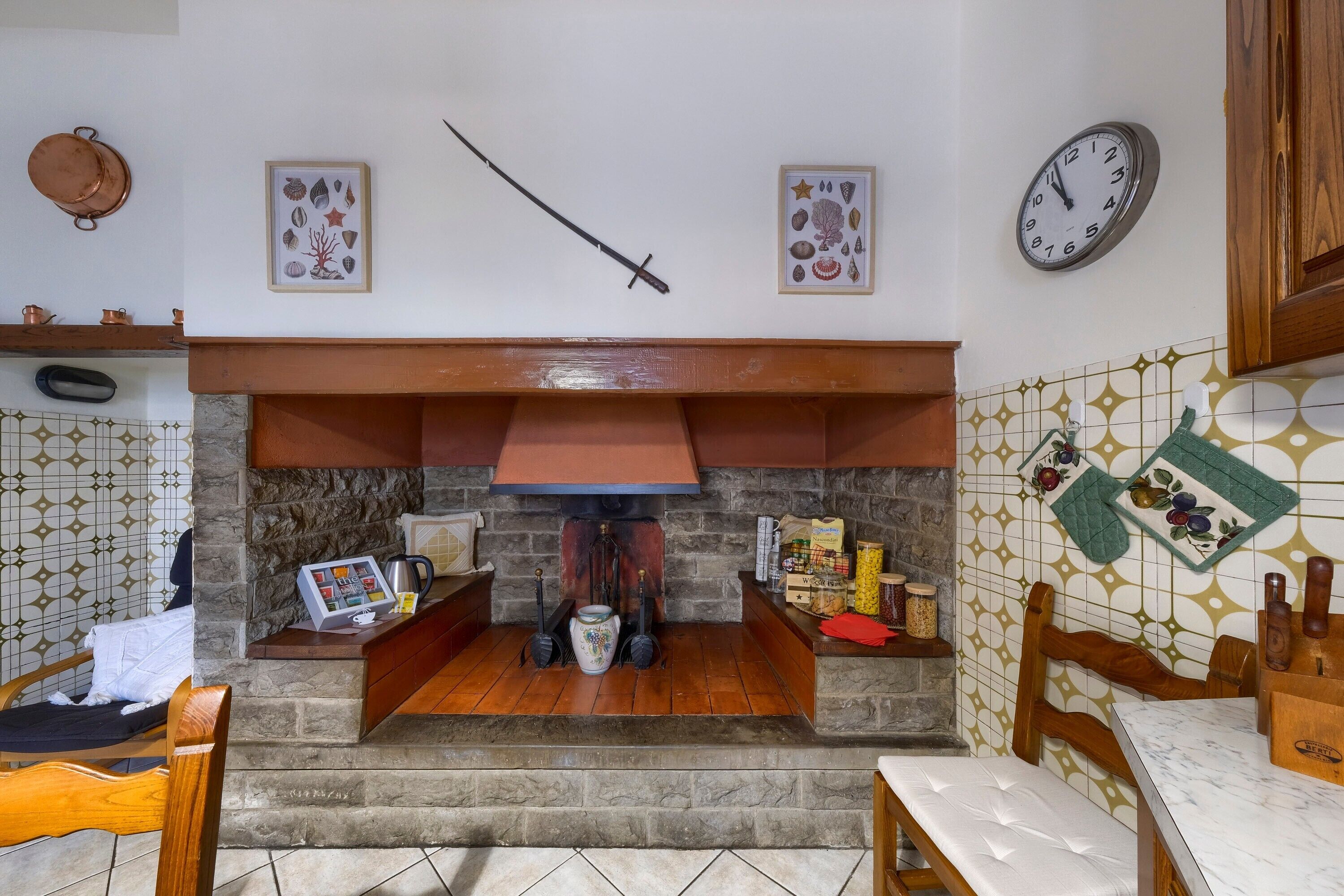 Una cocina con chimenea de piedra, muebles de madera y un reloj en la pared.