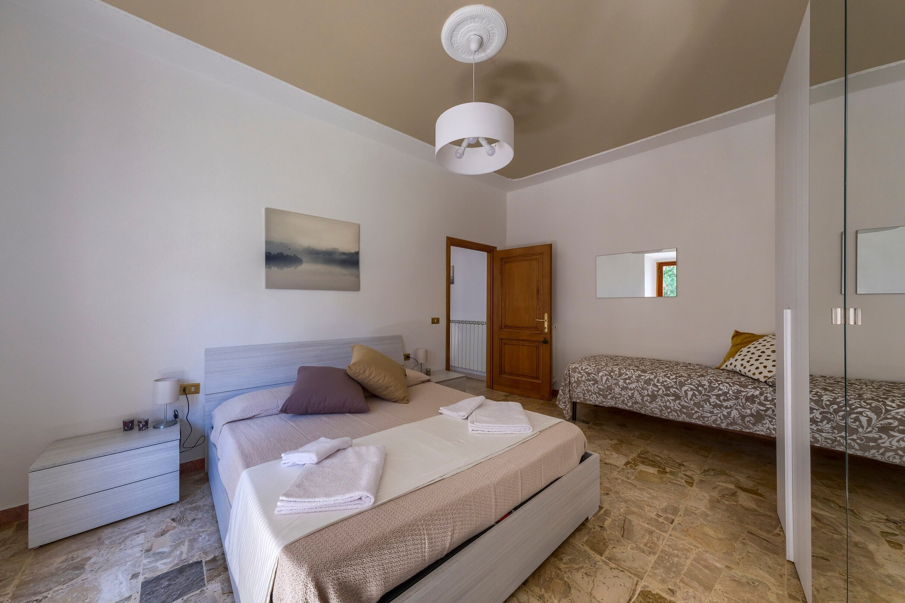 A bedroom with a bed, bedside table, lamp, and a view of the outside.