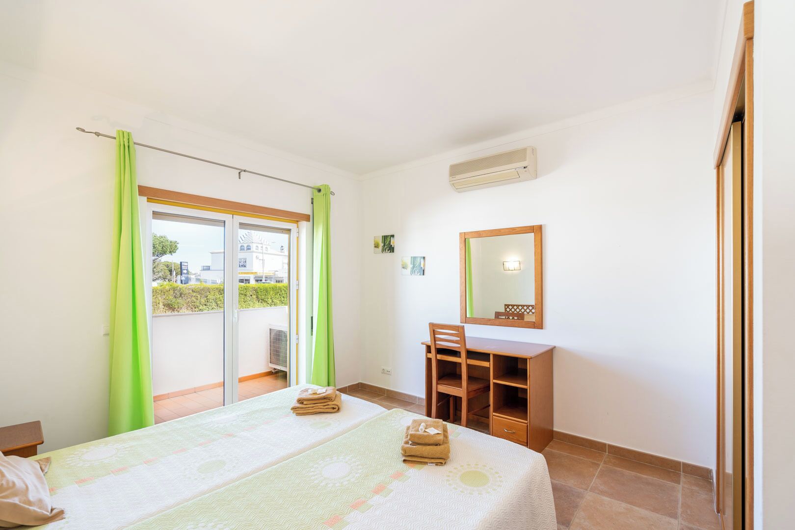 Un dormitorio con cama, escritorio, silla, espejo y ventana con cortinas.