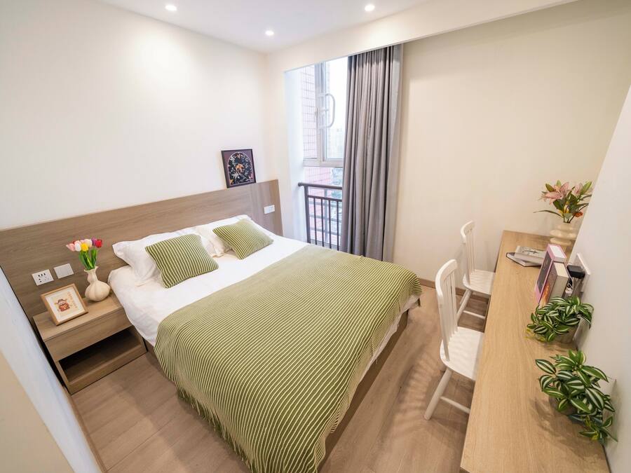 Un dormitorio ordenado con cama, mesita de noche y escritorio con sillas.