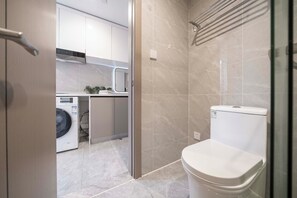 Une salle de bain moderne avec une douche à parois de verre, des toilettes et un lave-linge dans la pièce adjacente.