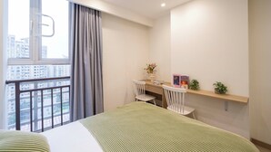 A modern hotel room with a large bed, a desk with two chairs, a small shelf with plants, and a window with a view of buildings. - Book and Bed-QuYang Road (Shanghai)