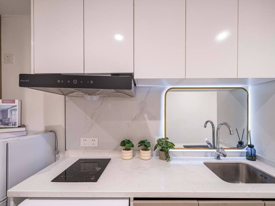 Uma cozinha moderna com armários brancos, forno embutido, pia de aço inoxidável e um pequeno balcão com plantas em vasos.