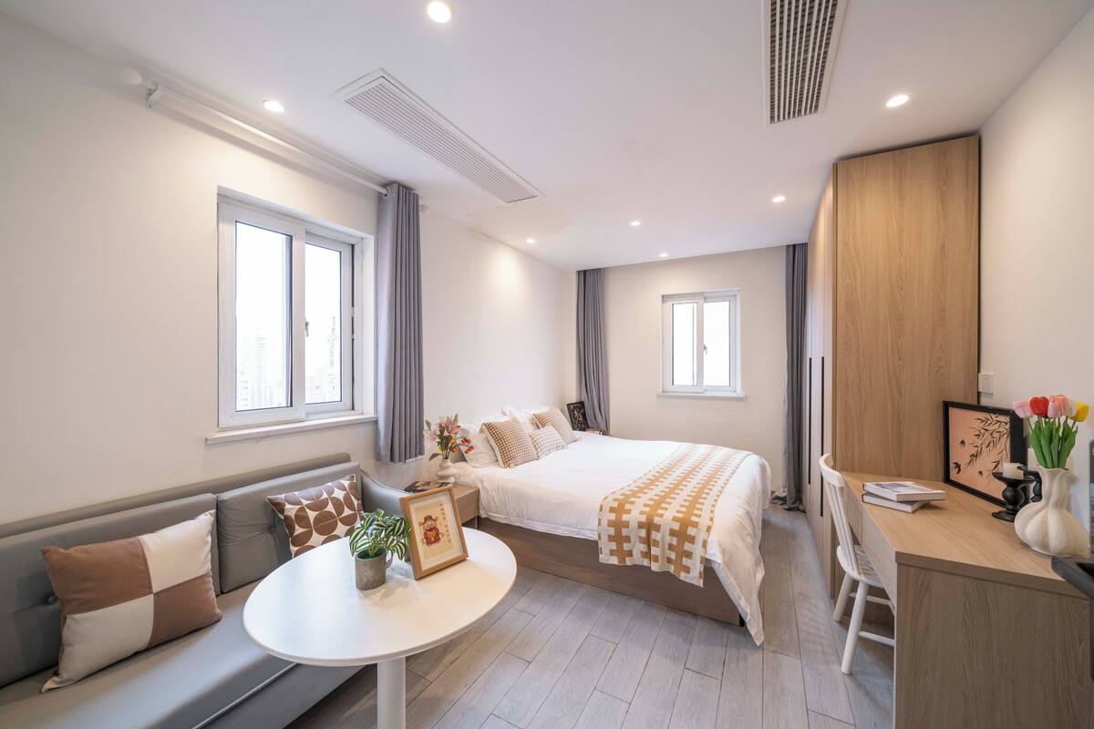A modern hotel room with a bed, a desk, a sofa, and a small table.