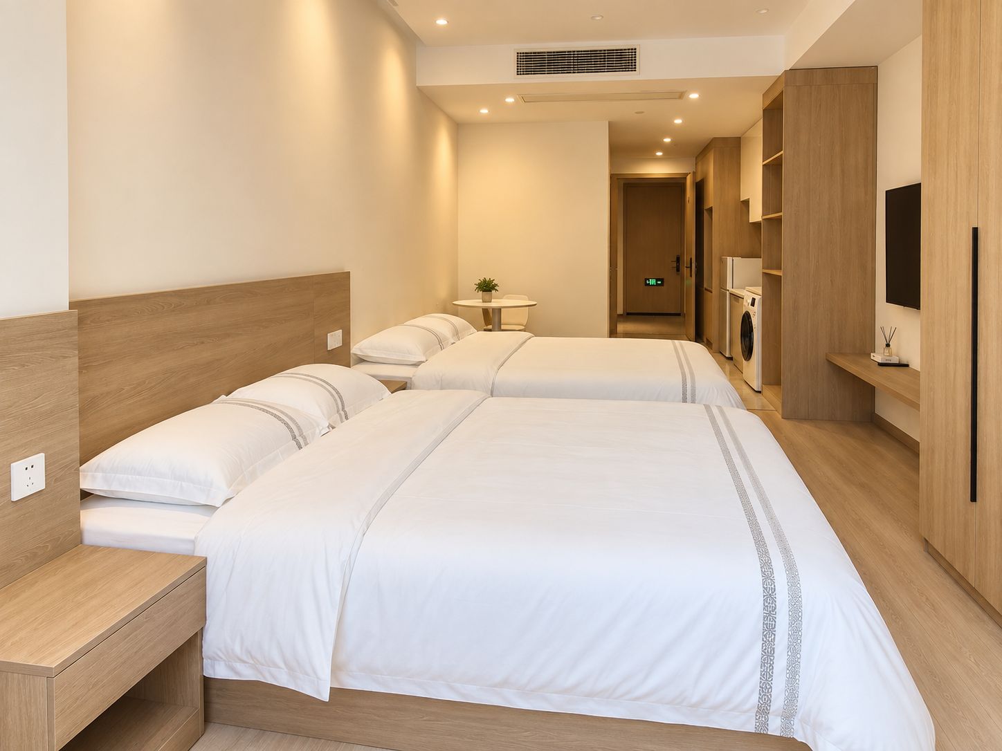 A hotel room with two beds, a bedside table, a small table with a plant, a TV, and a wardrobe.