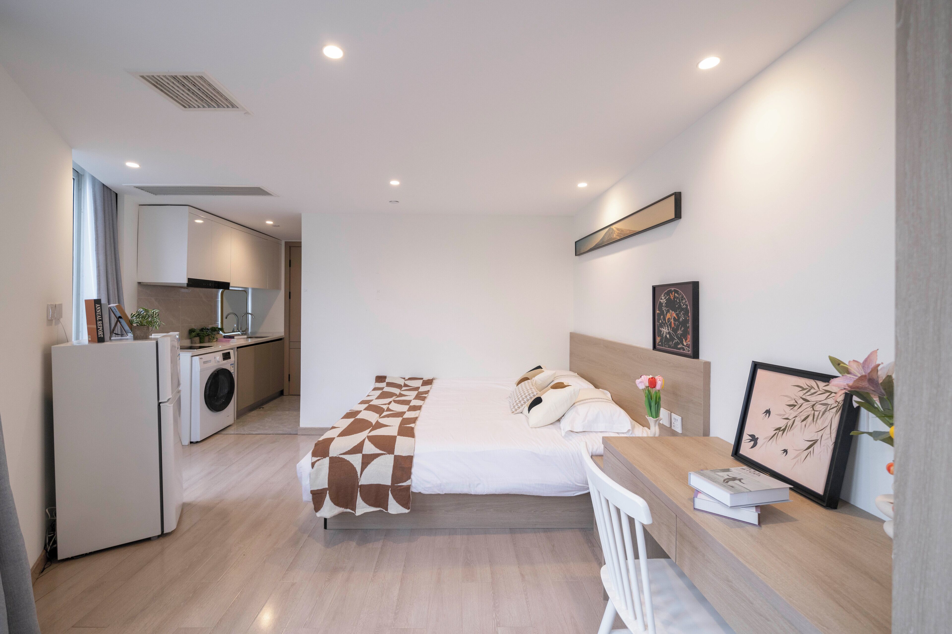 A modern hotel room with a bed, bedside table, and a small kitchenette.