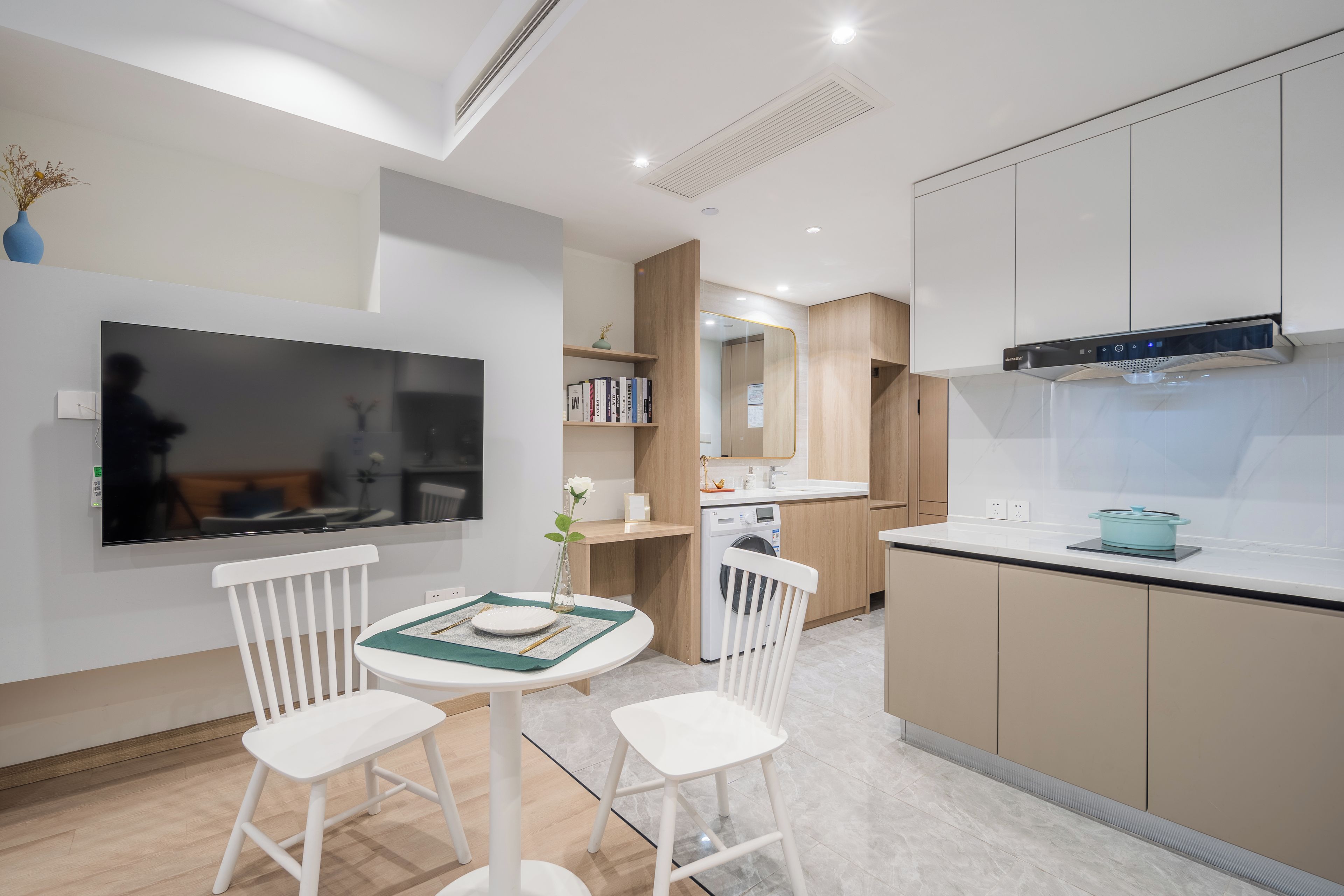 A modern kitchen with a built-in oven, a microwave, and a stove. There is a dining area with two white chairs and a small table.