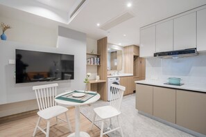 A modern kitchen with a built-in oven, a microwave, and a stove. There is a dining area with two white chairs and a small table. - Book and Bed-QuYang Road (Shanghai)