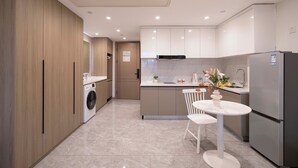 Une cuisine moderne équipée d’un lave-linge intégré, d’un coin repas avec une table et des chaises blanches, et d’un réfrigérateur en acier inoxydable.