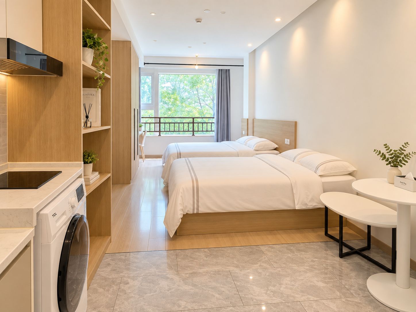 A modern hotel room with a washing machine, two beds, a round table, and a balcony with a view of trees.