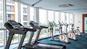 A gym with treadmills and stationary bikes, large windows, and a view of a building.