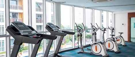 Ein Fitnessraum mit Laufbändern und Ergometer, großen Fenstern und Blick auf ein Gebäude.