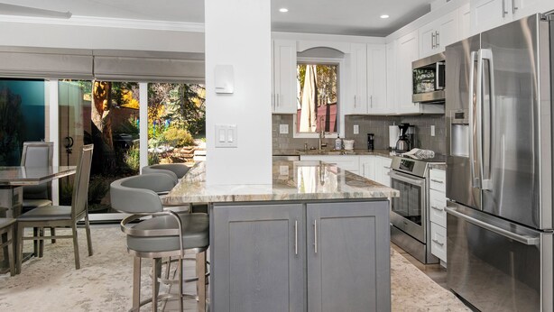 Una cocina moderna con una isla central, electrodomésticos de acero inoxidable y un comedor con taburetes de bar.