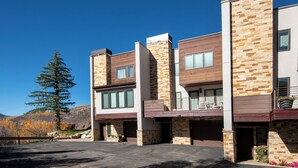 Un edificio moderno de varios pisos con fachada de piedra, ventanas grandes y un estacionamiento.