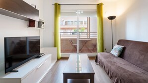 Ein modernes Wohnzimmer mit Flachbildfernseher, einer Couch, einem Couchtisch und einem Balkon mit Tisch und Stühlen.