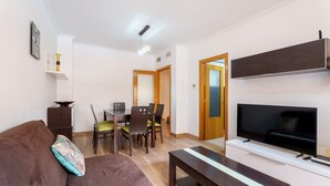 Ein Wohnzimmer mit einer Couch, einem Couchtisch, einem Fernseher, einem Esstisch mit Stühlen und einer Holztür.