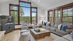 A spacious living room with a large TV, comfortable seating, and large windows offering a view of the outdoors. - Modern Luxury | Mountain Views | Hot Tub + Shuttle - Cherrybrook Chalet (Breckenridge)