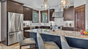 A modern kitchen with dark wood cabinets, stainless steel appliances, and a marble island with bar stools. - Modern Luxury | Mountain Views | Hot Tub + Shuttle - Cherrybrook Chalet (Breckenridge)