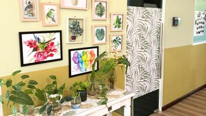 En hall med ett vitt konsolbord där olika krukväxter står och på väggen hänger inramade botaniska konstverk.