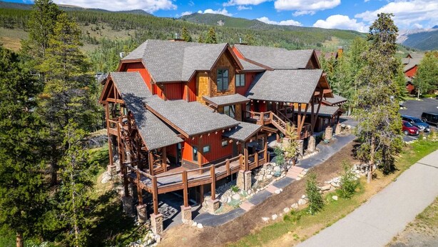 A multi-story log cabin with a deck and a stone pathway leading to the entrance.